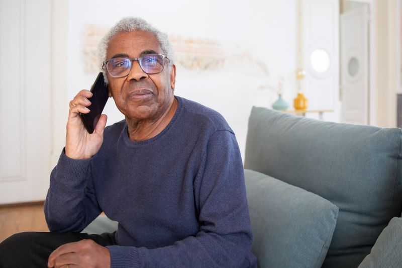An elderly man taking a phone call on his couch