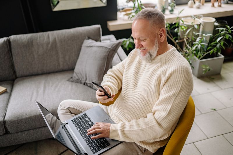 A man smiling at his phone with a laptop on his knees