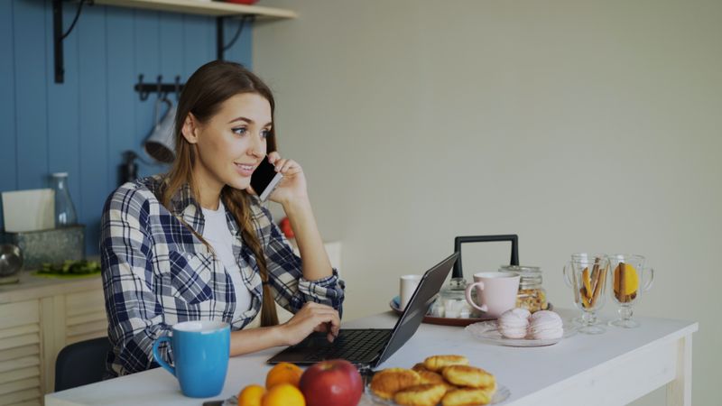 A woman on the phone at her kitchen table
